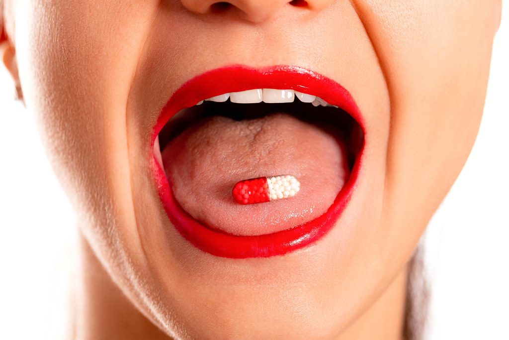 Close-up, medicine capsule on woman's tongue