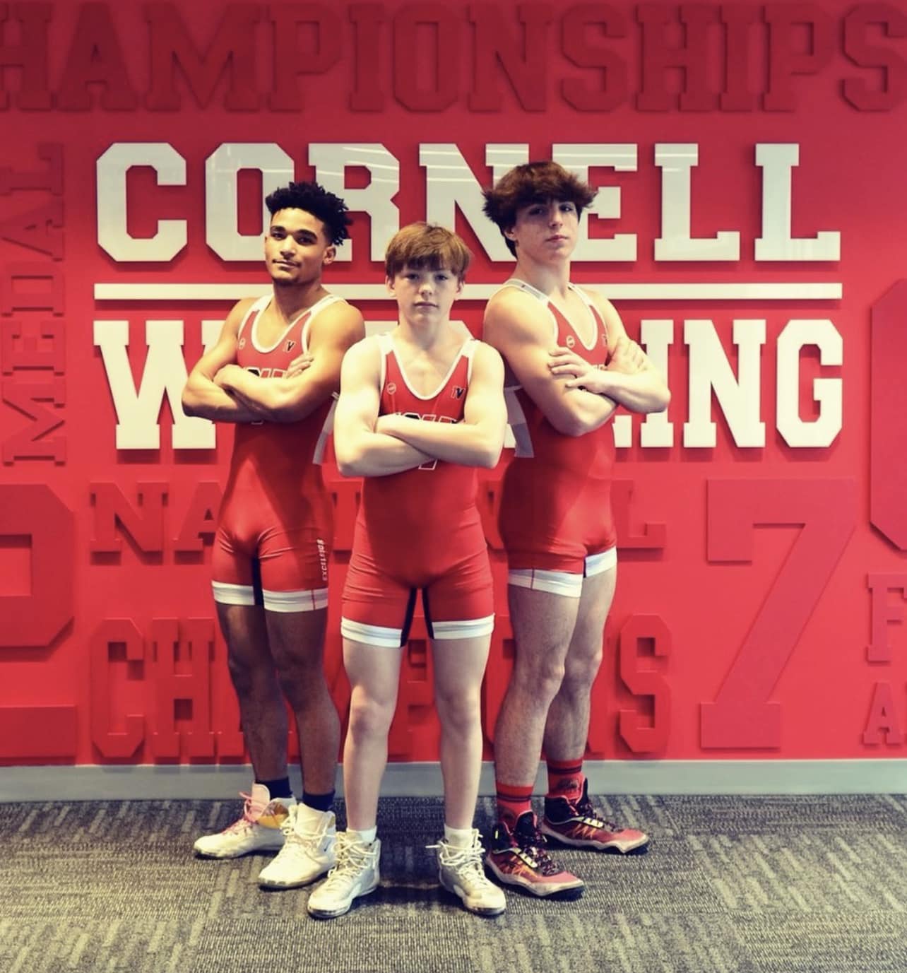 three Ithaca High wrestlers in front of a Cornell wrestling sign