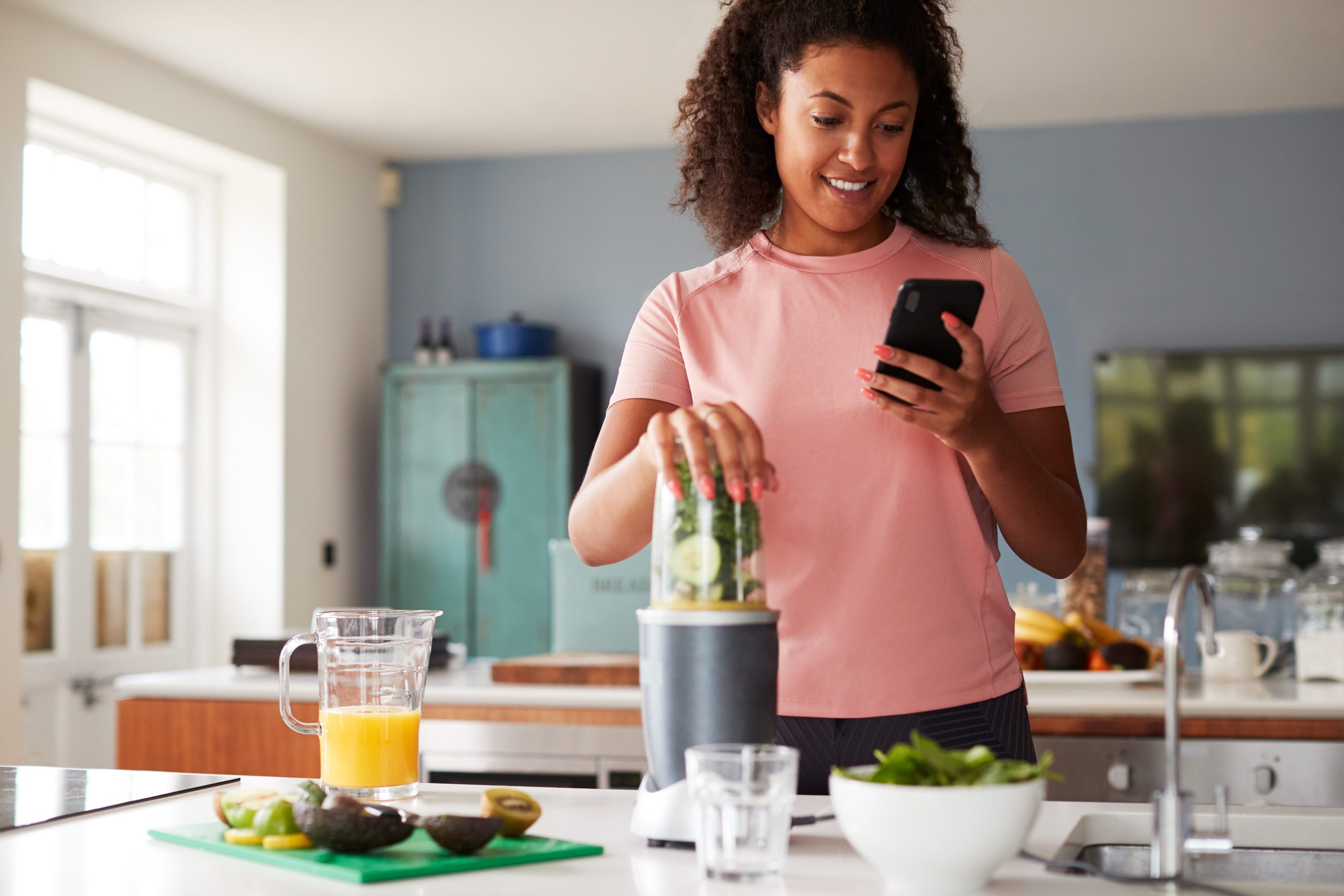 Woman using fitness tracker to count calories for post workout juice drink she is making.