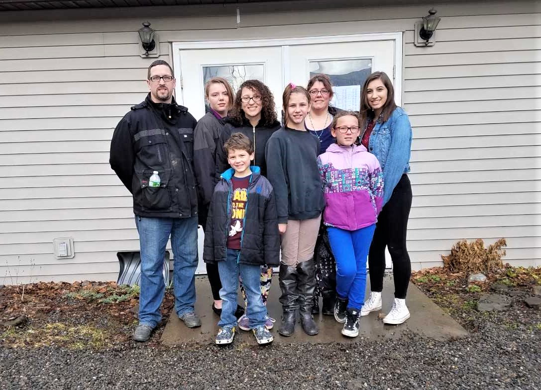 The Stone Family standing in front of the Joyce Crouch Benevolence Building, 701 S. Main St., home of the Groton Food Providers food pantry. Front row, left to right: Jeremiah Stone, Michaela Stone, Olivia Stone. Back row, left to right: Mike Stone, Arianna Stone, Cassandra Stone, Jess Stone, Lila Stone.