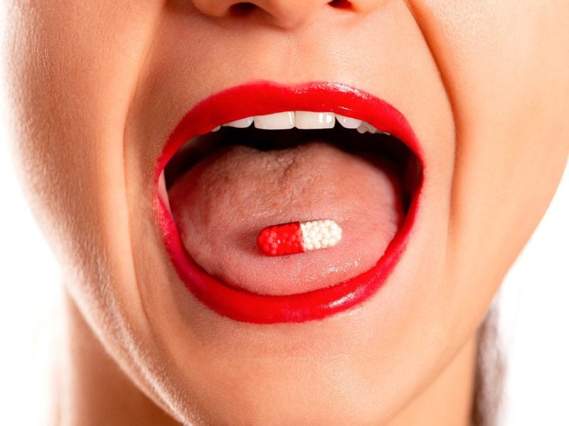 Close-up, medicine capsule on woman's tongue