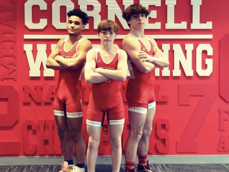 three Ithaca High wrestlers in front of a Cornell wrestling sign