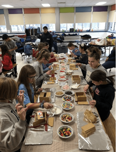 students gathered at cafeteria tables building gingerbread houses.