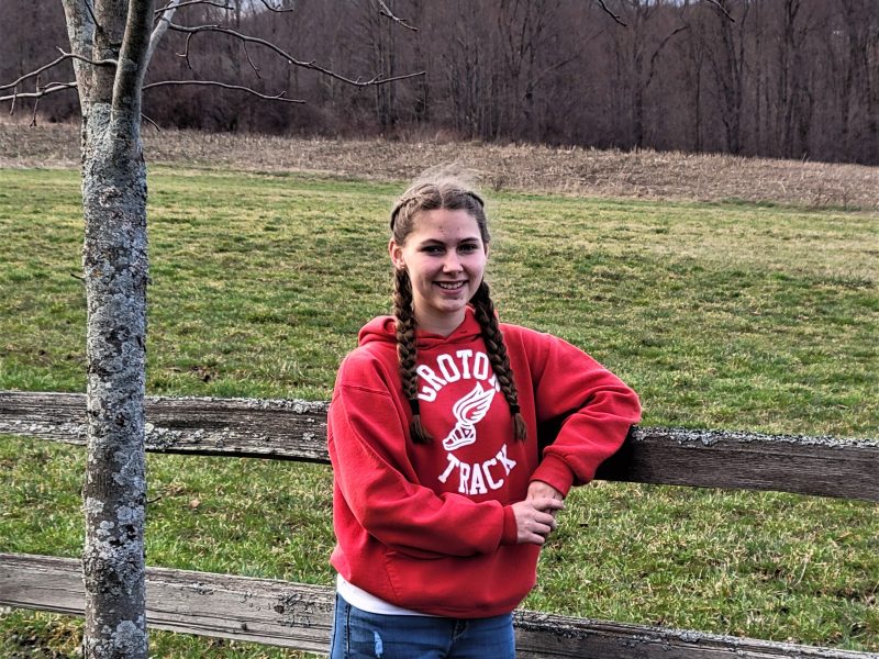 Addie Clore leans on a fence in front of an open field
