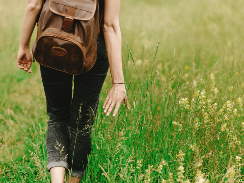 woman walking through a field with a backpack on