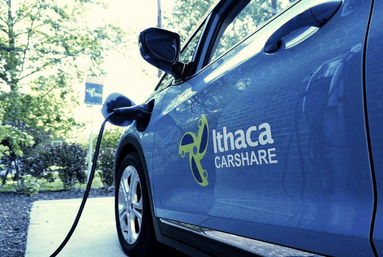 an electric car charging. The sticker on the side is the Ithaca Carshare logo to show that the car belongs to the carshare.