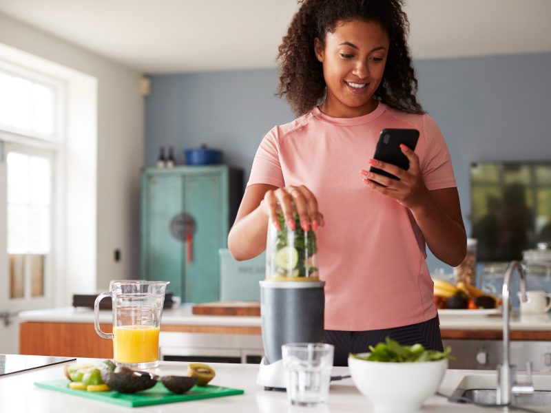 Woman using fitness tracker to count calories for post workout juice drink she is making.