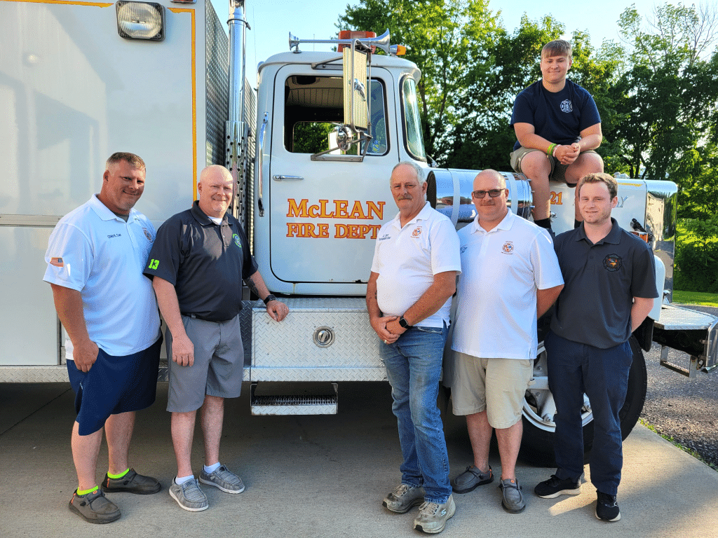 By Linda Competillo
The Carr family of McLean represents a legacy of four generations of firefighters, which began with the late Edward L. Carr. Pictured here (left to right) are brothers Ken and Larry, Dell (son of Edward), Calvin (twin brother of Ken), and Damon (son of Larry), with Ken’s son, Ethan, sitting atop the McLean Fire Department’s 1974 Brockway fire truck, which is still operational.