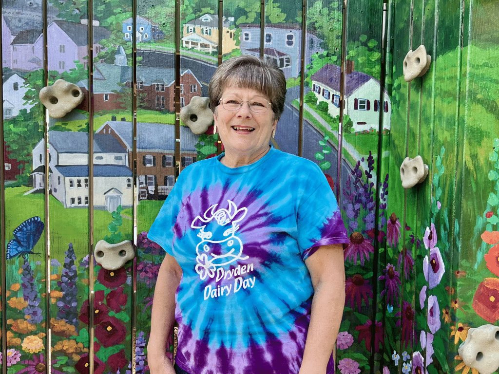 Photo by Jaime Cone Hughes 
Brenda Carpenter, Dryden Dairy Day longtime organizer, stands in front of a mural at Montgomery Park, where the festival is held. Carpenter is the most recent recipient of our Hometown Heroes Award. 