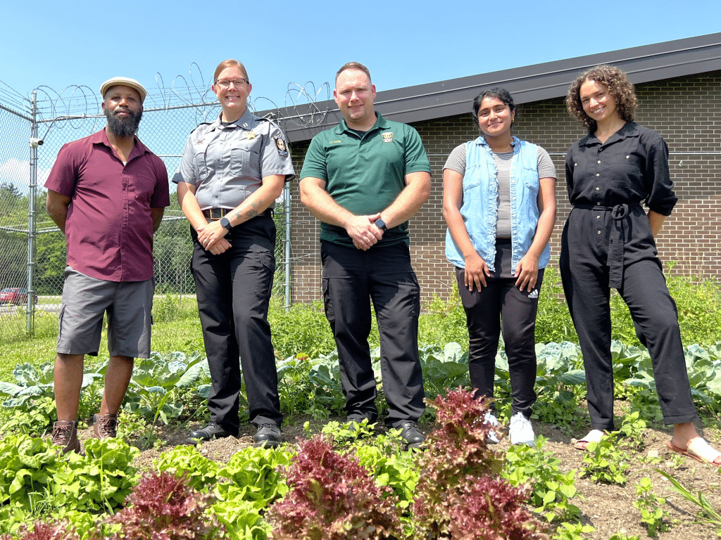 Photo by Jaime Cone Hughes
(From left to right): Taili Mugambee, director of Ultimate Reentry Opportunity (URO), Captain Lauran Harrison, corrections division supervisor at the Tompkins County Sheriff’s Department, Seth Case, lieutenant at the Tompkins County Sheriff’s Department, Anya Gowda, a Cornell University student interning for URO, and Sadie Crusade, operations and administrative manager for URO, at the Jail Garden at the Tompkins County Jail in Ithaca.