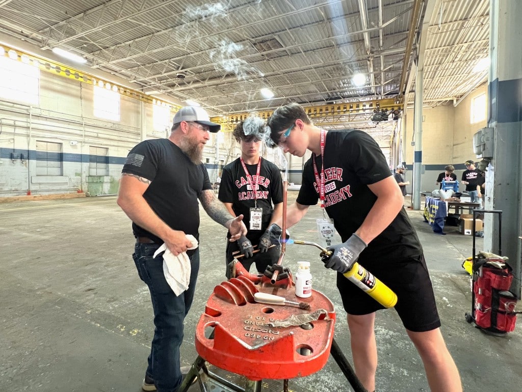 Photo by Jaime Cone Hughes
Tommy Hayward (left), training coordinator for UA Local 81 plumbers, steamfitters and HVAC technicians, supervises Groton High School student Nick Sill as he welds two pipes together at SouthWorks Thursday while Graeme Crispbell, also a Groton High School student, looks on.
