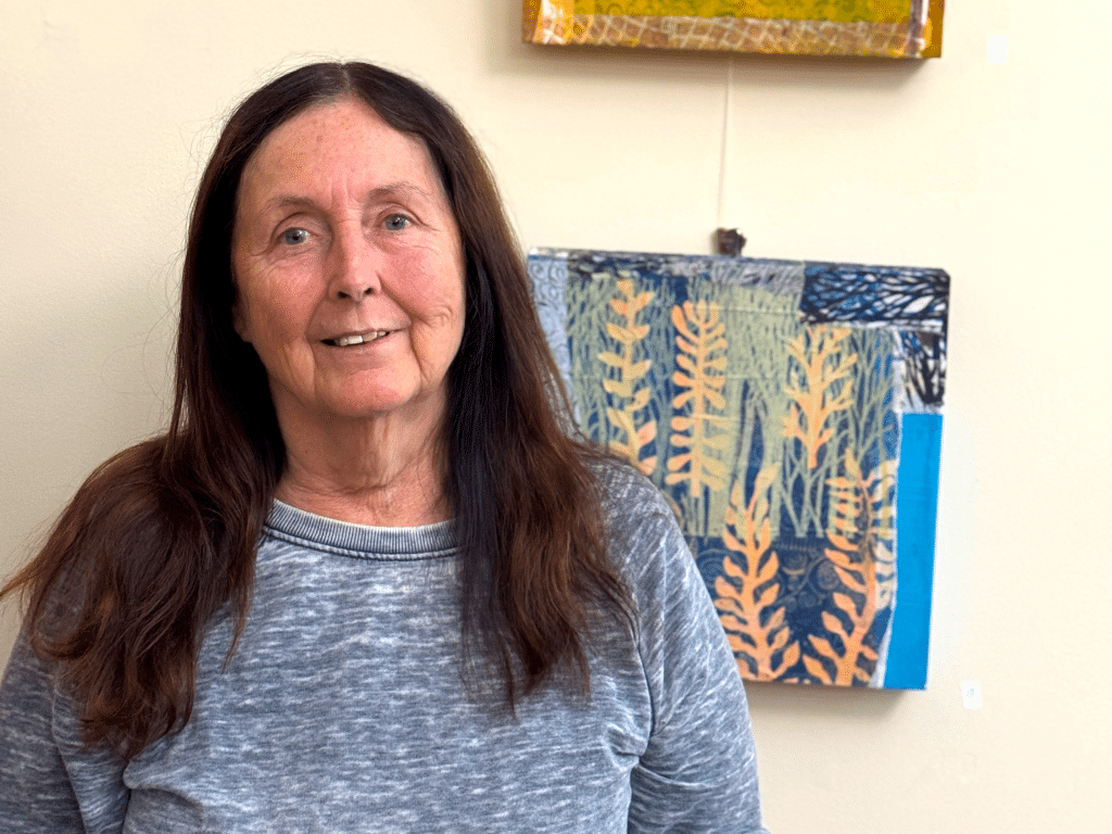 Artist Dianne Lynne with her collages hanging behind her. Her latest showing will have a reception at the Ulysses Philomathic Library Sept. 27 from 10:30 to 11:30 a.m. There will be refreshments from 11:30 a.m. to 1:30 p.m., as well as a printmaking demonstration, with participants invited to make a print.