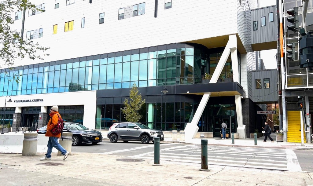 By Jaime Cone Hughes 
East Green Street in Ithaca, with the entrance to the Ithaca Downtown Conference Center on the left. On the right, residents of Asteri Ithaca apartments enter through a separate entrance in the alley near Cinemopolis. An enclosed walkway from the apartments to the Green Street parking garage provides a second entrance for residents. The conference center, which takes up the first three floors of the building, is suing Vecino Group for $5 million in damages, claiming that Vecino’s mismanagement of the apartments has caused unsafe, unsanitary conditions that led to the loss of conference center clients. 